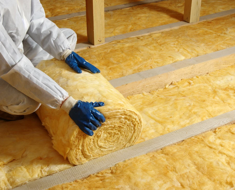 Ouvrier en combinaison bleue installant de l'isolant thermique jaune dans les combles d'une habitation