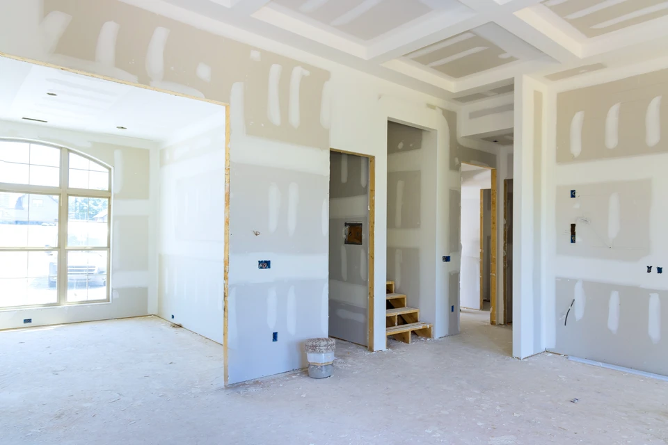 Chantier de construction intérieur avec ouvrier installant l'isolation thermique entre montants métalliques d'une cloison