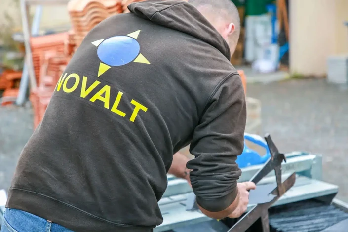 Ouvrier couvreur en tenue de sécurité orange et bleue travaillant sur une toiture en pente