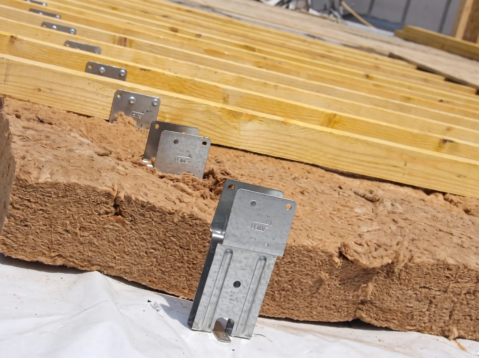 Ouvrier en combinaison grise installant de l'isolation thermique jaune entre les solives d'un plafond dans un bâtiment en construction
